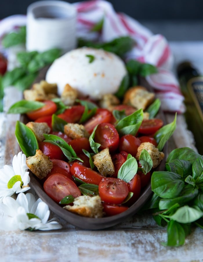 side view of the burrata caprese salad showing close up of the tomatoes laced in basil and crouton with burrata cheese