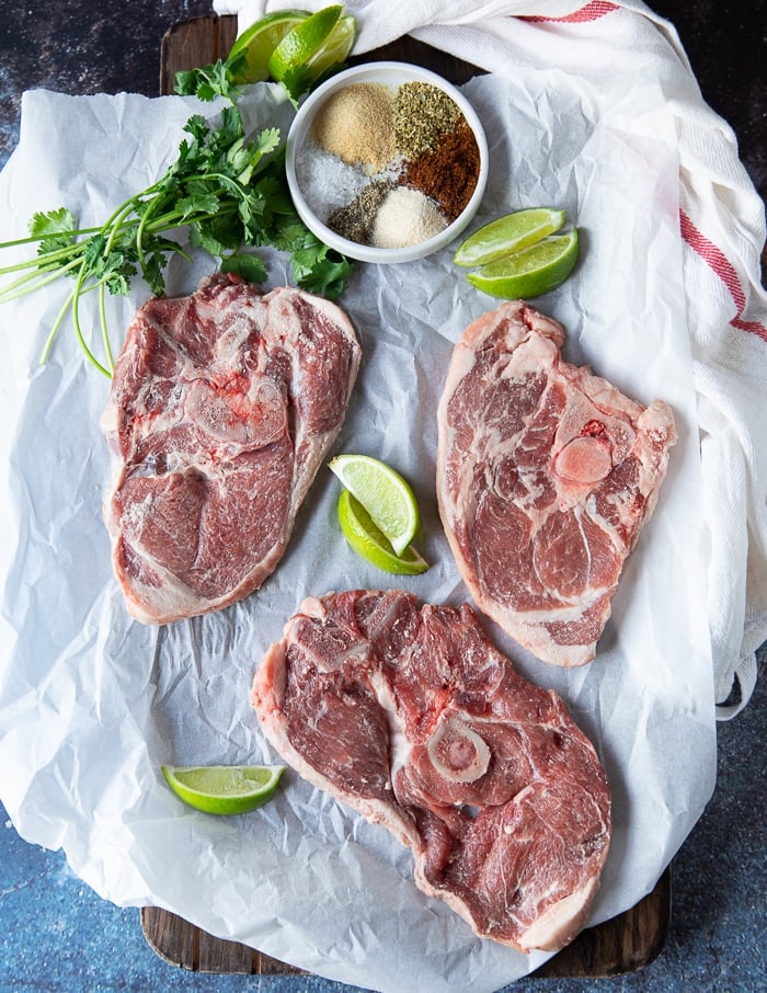 chunks of meat and a bowl of spice on a board to make the carne asada