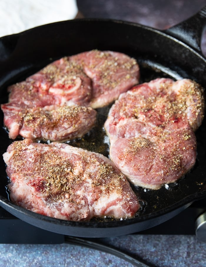 Steak being seared in a hot cast iron skillet with some oil