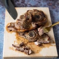 Steak being cut up in a wooden board using a for and a knife into 1 inch cubes for carne asada recipe