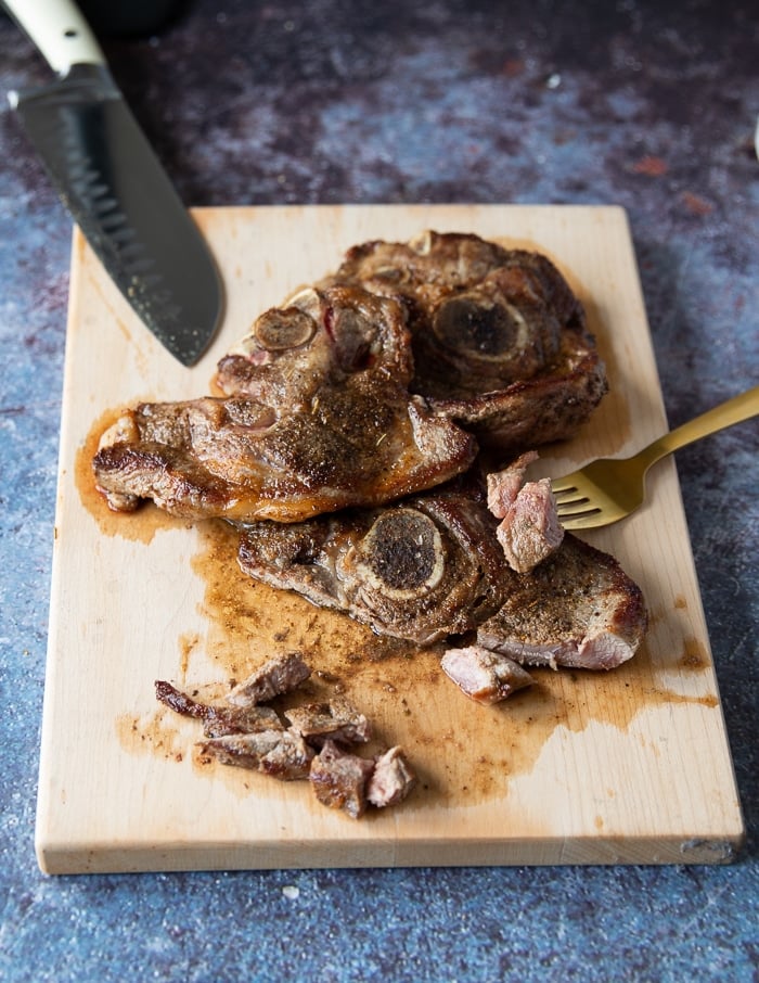 Steak being cut up in a wooden board using a for and a knife into 1 inch cubes for carne asada recipe