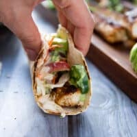 A hand holding the finished mahi mahi tacos sideways showing the mahi mahi fish, fish slaw, avocado and poblano sauce