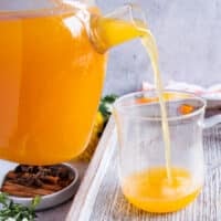 A glass jar pouring fresh homemade apple cider into a class cup