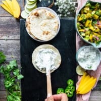 Assembling the tacos recipe: hand spreading some herb sour cream over a tortilla