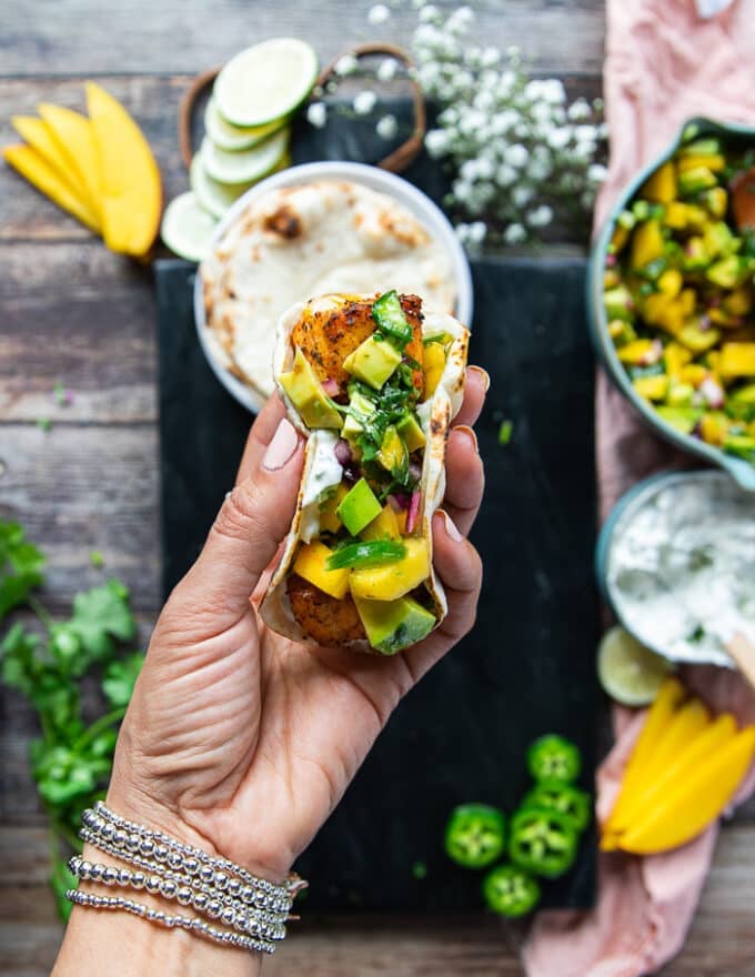 A hand holding a finished salmon taco showing the cooked salmon and salsa