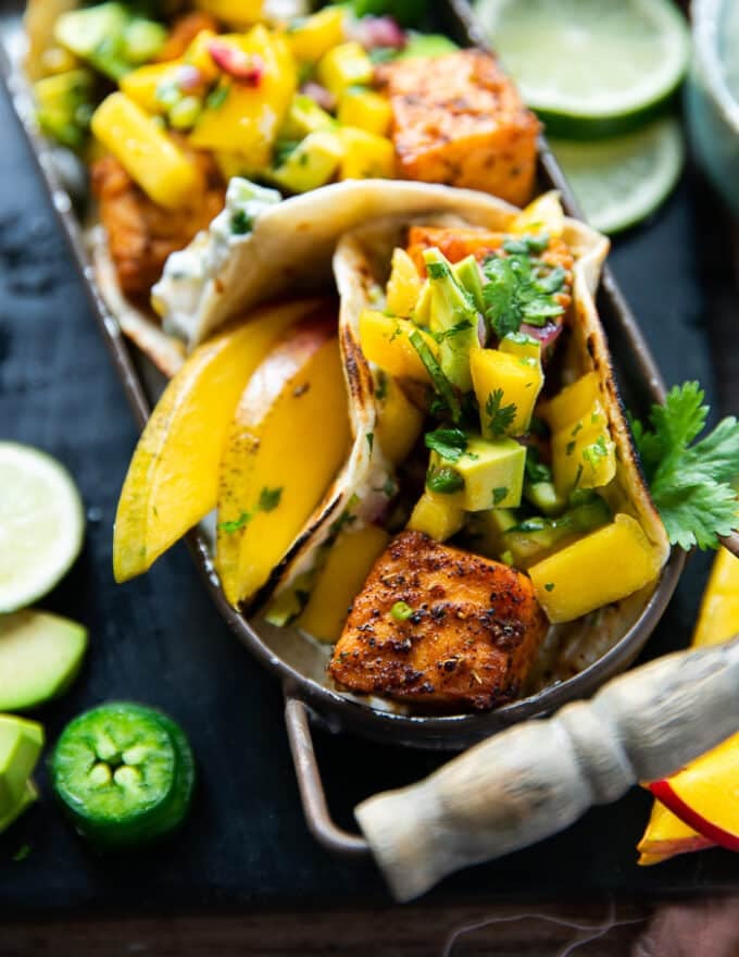 perfect salmon taco with white sauce, avocado salsa surrounded by lime wedges and jalapeno slices
