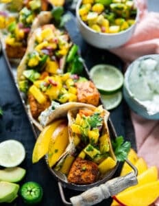 close up of salmon tacos on a plate with some lime slices around, some sour cream and avocado salsa