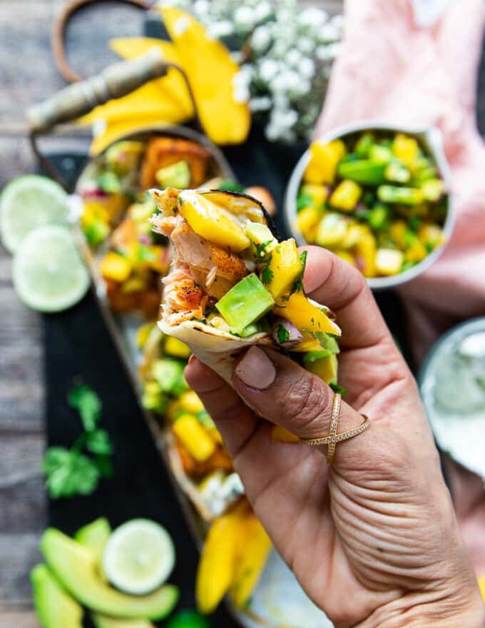 A hand holding a bitten salmon taco to show how the salmon taco recipe blends together 