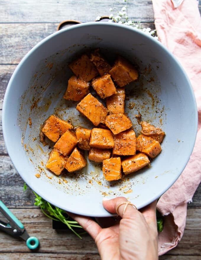 Salmon chunks coated in spice and olive oil in a large bowl and ready to cook for salmon tacos