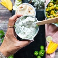 a hand holding a bowl of sour cream ready with herbs