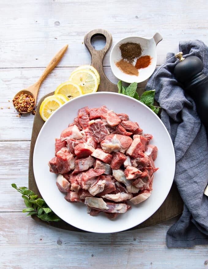 A plate of lamb chunks to make lamb stew surrounded by a bowl of turkish spices to spice up the lamb