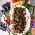 A large plate of lamb stew served over eggplant and yogurt to make Ali Nazik recipe, surrounded by red chilies, green chilies, lemon wedges, turkish pepper flakes, bread and tomatoes