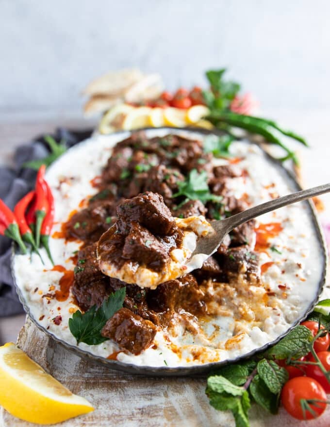 A spoon scooping some lamb stew from the plate and scooping some yogurt and eggplant with it