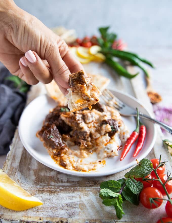 A hand scooping with bread some lamb stew along with the eggplant yogurt mix to serve