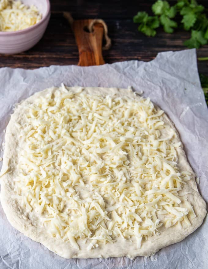 making the pizza: a layer of cheese is added over the raw pizza dough