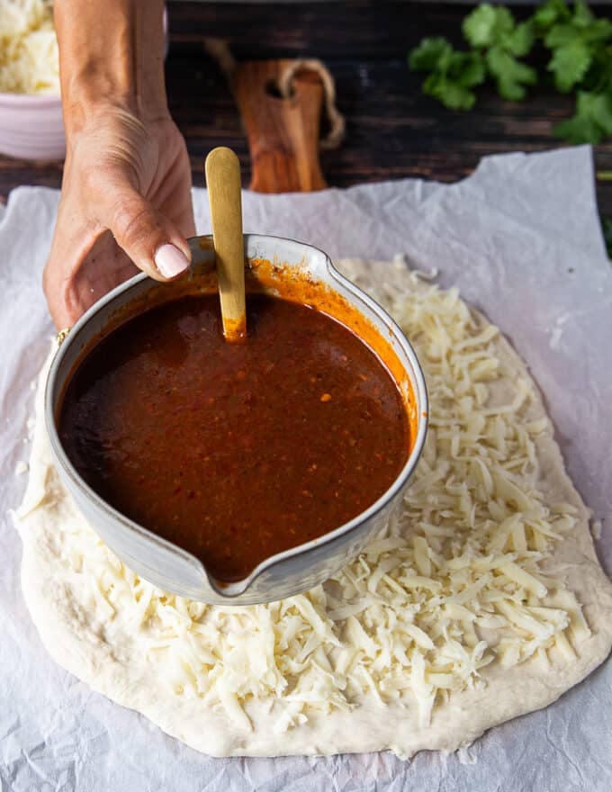 A hand holding the birria stew and ready to add it over the cheese