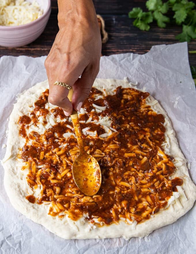 a hand holding a spoon spreading the birria sauce over the cheese