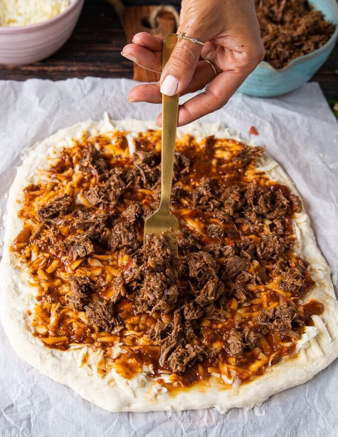 a hand holding a fork and adding the burria meat over the sauce on the pizza dough