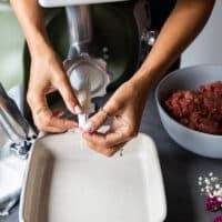 A hand holding the casings attached to the sausage maker to show the type of casing to make sausage links