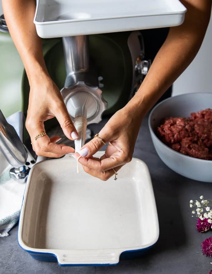 A hand holding the casings attached to the sausage maker to show the type of casing to make sausage links