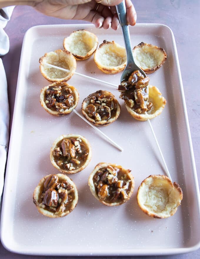 The cooked pie crusts are placed on a baking sheet and the pecan pie filling is divided among them