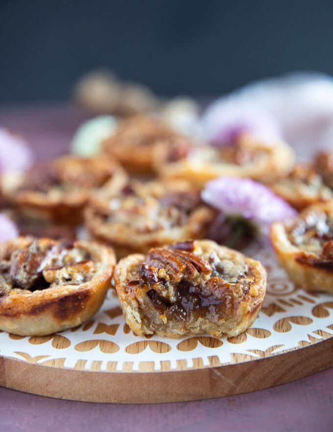 A bitten mini pecan pie on a wooden board showing how luscious the filling is