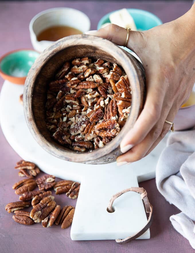 A hand holding a bowl of a mortar and pestle with whole pecans ready to coarsely crush some