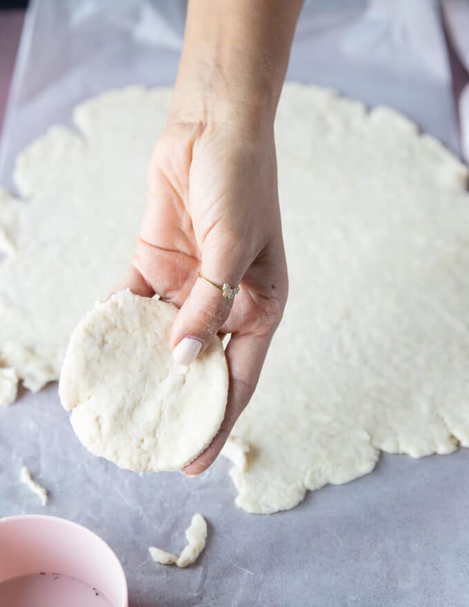 A hand rolling out the homemade pie dough and cutting out rounds of it
