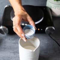 A hand adding some flour into a jar of half n half to make turkey gravy