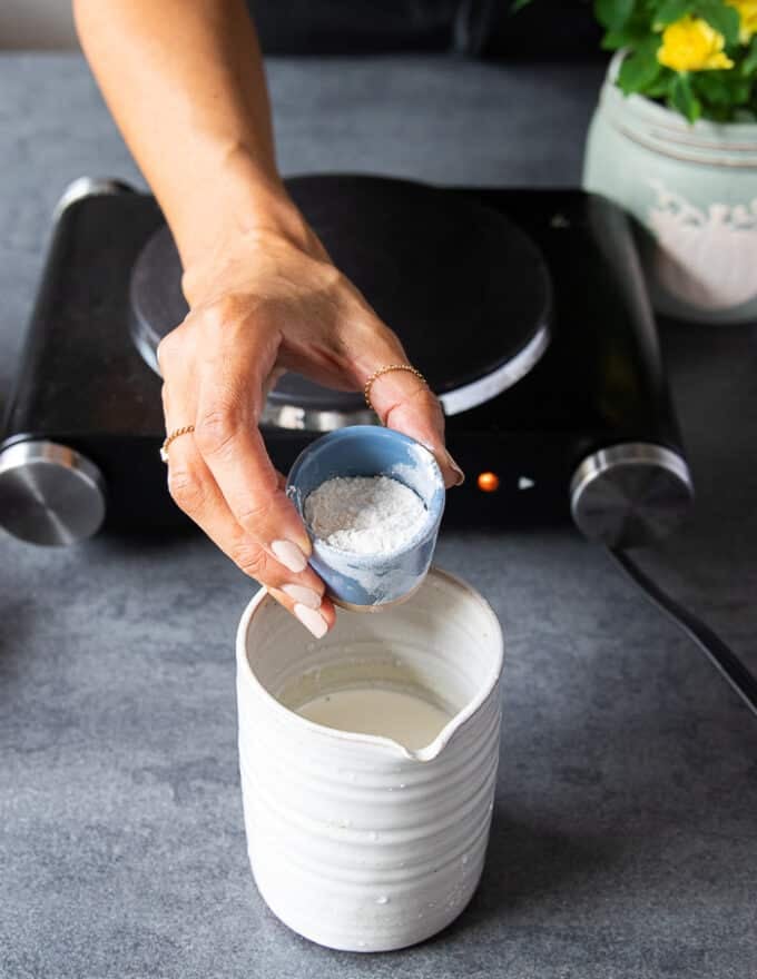 A hand adding some flour into a jar of half n half to make turkey gravy