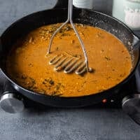 A hand mashing the ingredients in the gravy using a potato masher