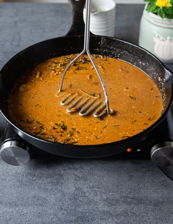 A hand mashing the ingredients in the gravy using a potato masher