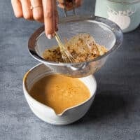 A hand straining the turkey gravy in a fine mesh strainer over a bowl