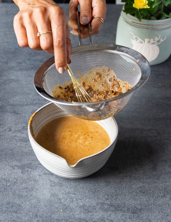 A hand straining the turkey gravy in a fine mesh strainer over a bowl 