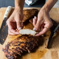 A hand holding a piece of turkey tenderloin just sliced and showing how juicy it is out of the oven