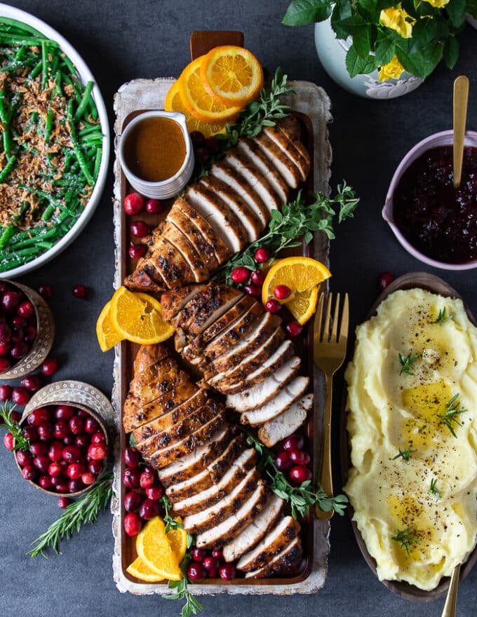 A large thanksgiving table setup with turkey tenderloin sliced on a board, surrounded by cranberries, mashed potatoes and green beans casserole