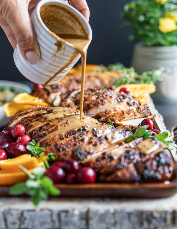 A hand pouring the gravy over the sliced turkey tenderloin recipe