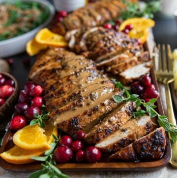 Gravy drenched turkey tenderloin recipe on a platter with orange slices and cranberries close up