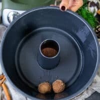a sprayed bundt pan and a hand arranging the dipped and coated cinnamon roll monkey bread pieces at the bottom of the pan