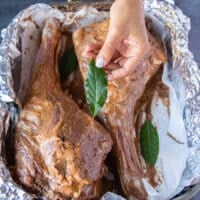 a hand holding a. bay leaf adding it to the roast lamb