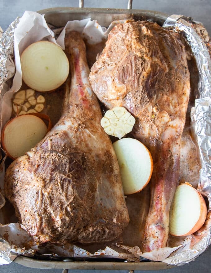 marinated leg of lamb in a roasting pan and ready to roast with adding onions, bay leaves, stock and whole spices