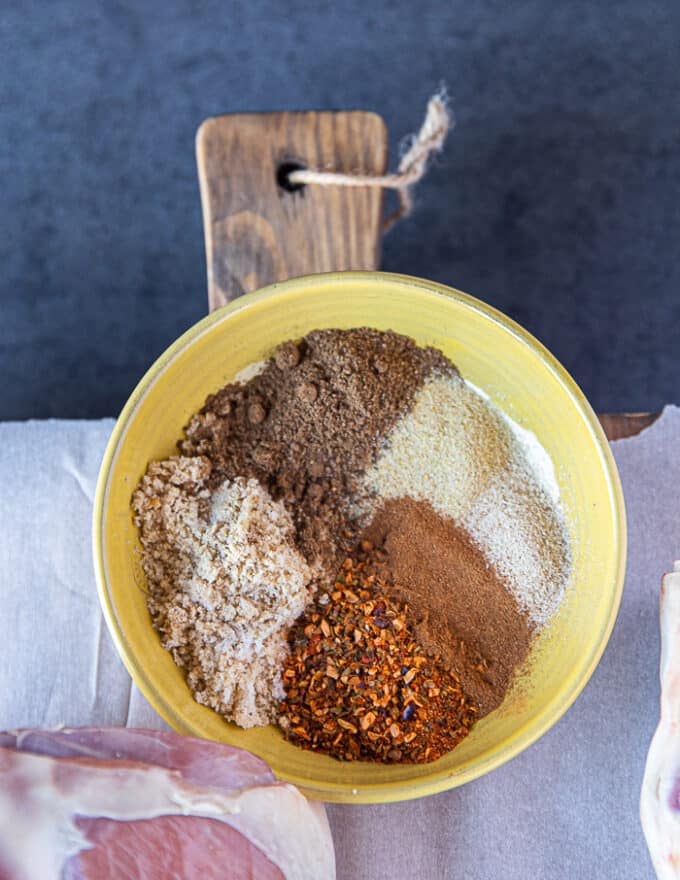 A plate with a variety of dry spice rub for the leg of lamb including salt, pepper, turkish pepper flakes, paprika, cinnamon, brown sugar, garlic powder, 
