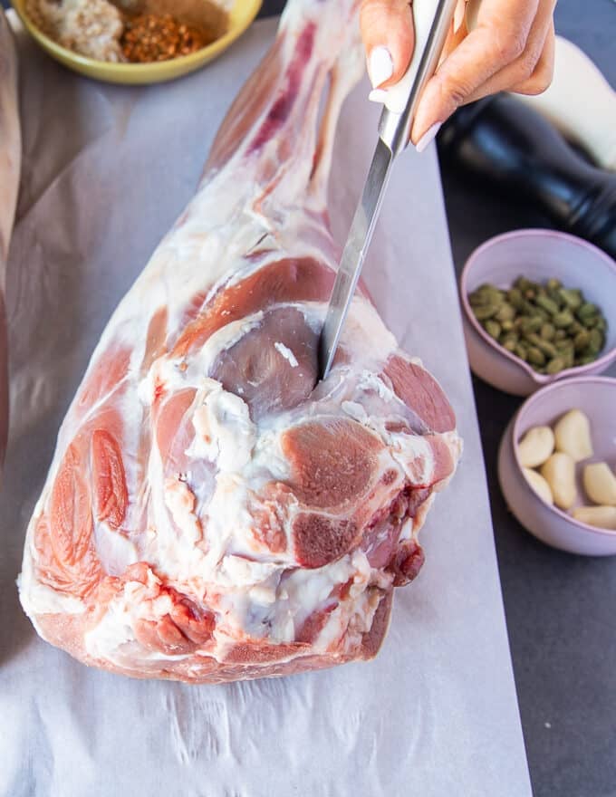 A hand using a sharp paring knife making slits along the leg of lamb 