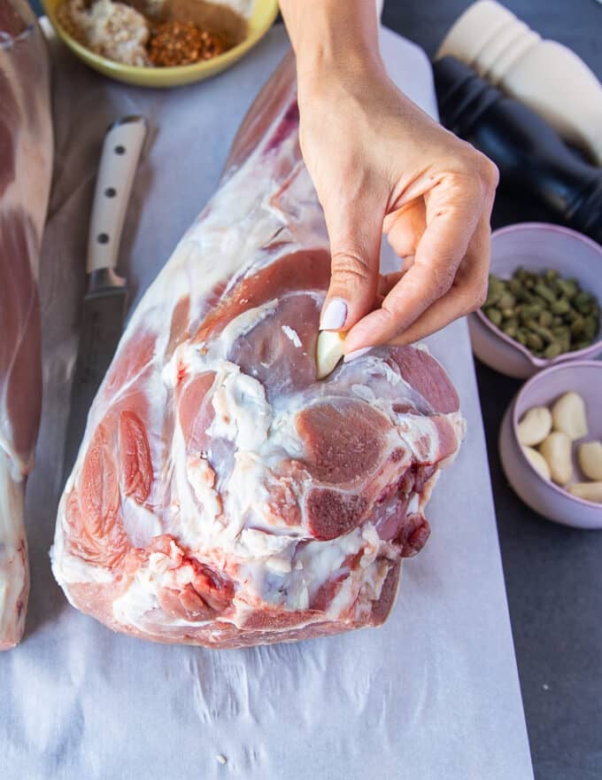 A hand inserting a garlic clove in the slit cut up in the leg of lamb to flavor it