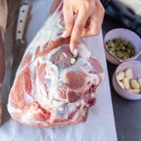 A hand pressing down the garlic , cardamoms and whole peppercorns into the lamb slits