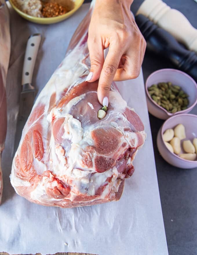 A hand pressing down the garlic , cardamoms and whole peppercorns into the lamb slits 