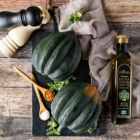 Two washed and cleaned acorn squashes on a black board surrounded by olive oil, salt and pepper shakers