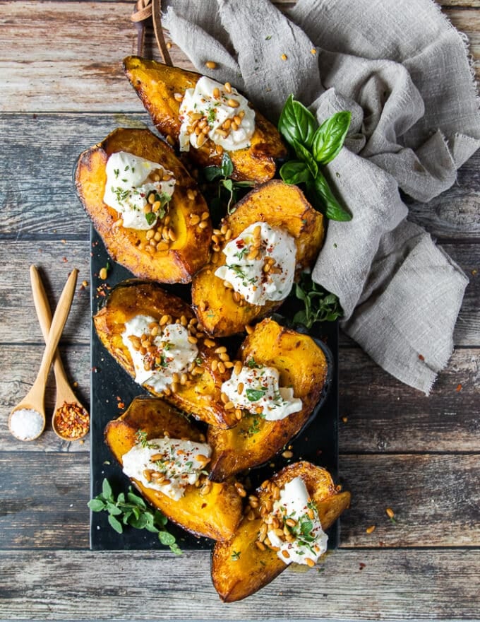 final plate of roasted acorn squash topped with burrata cheese, pine nuts, olive oil and fresh herbs surrounded by a tea towel and fresh herbs