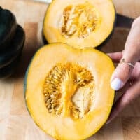 A hand holding a cut up piece of acorn squash showing the inside flesh and seeds before scooping