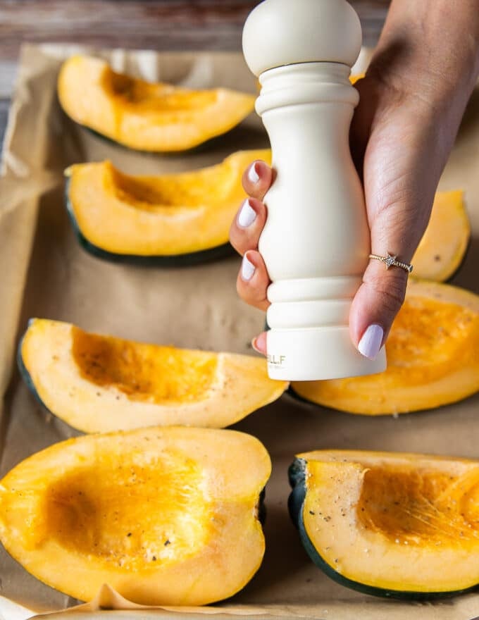 A hand holding a salt shaker and seasoning the squash wedges